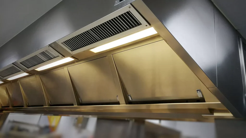 Expert technician cleaning commercial kitchen hood to prevent grease buildup.